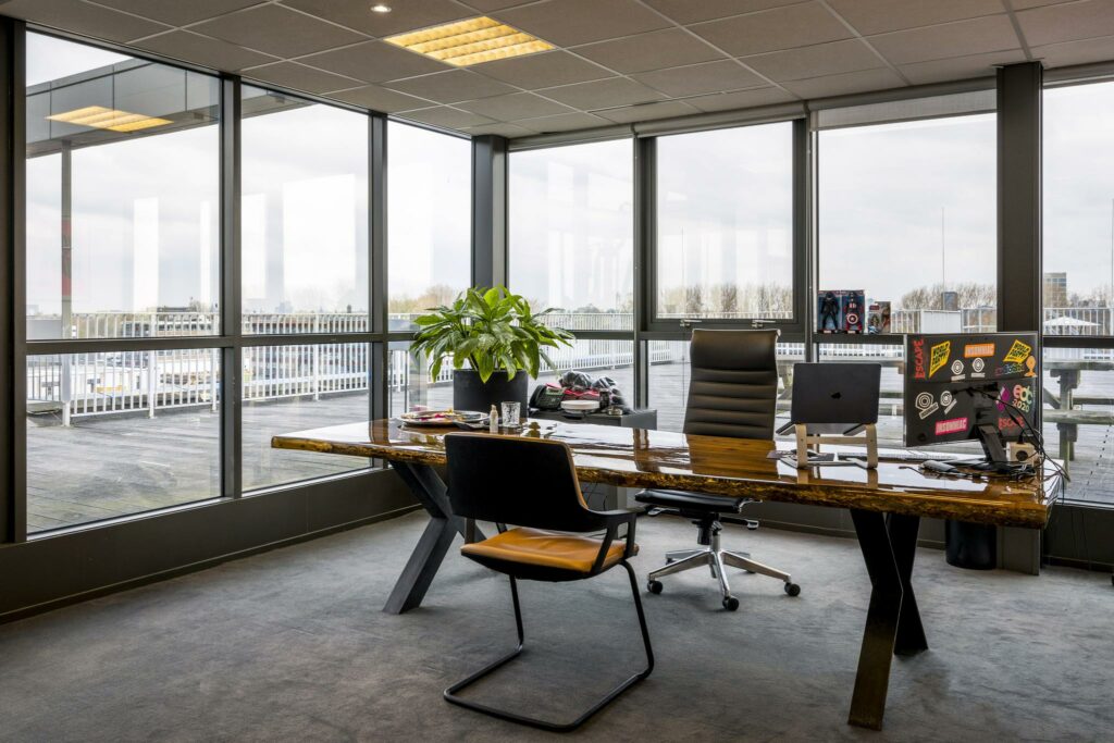 Modern kantoor met houten bureau, grote ramen en uitzicht op het buitenterras aan de Anthony Fokkerweg.